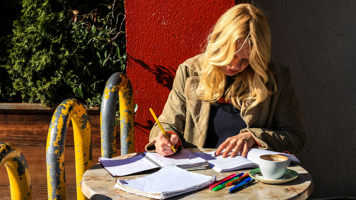 Mujer escribiendo en sus cuadernos en la mesa de una terraza