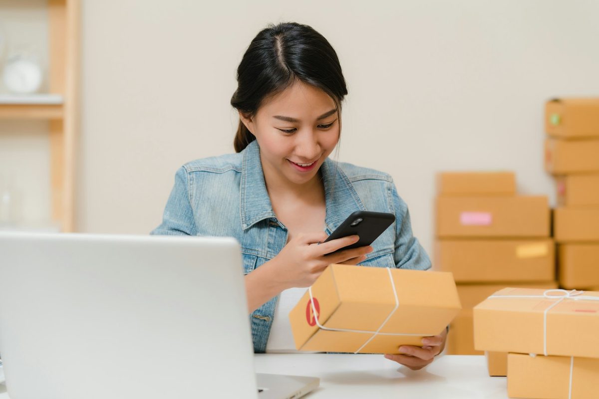 Vendedora preparando paquetes mientras mira el móvil