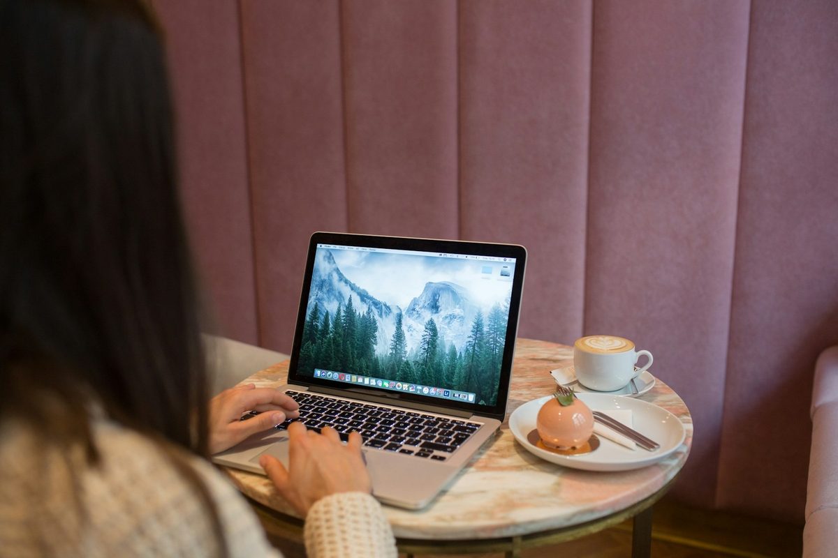 Persona trabajando con un portátil en la mesa de una cafetería, vista desde atrás
