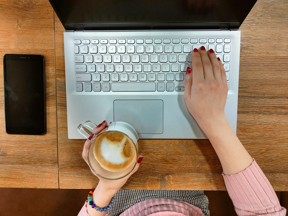 Portátil, móvil y una taza de café sobre una mesa de madera, vistos desde arriba