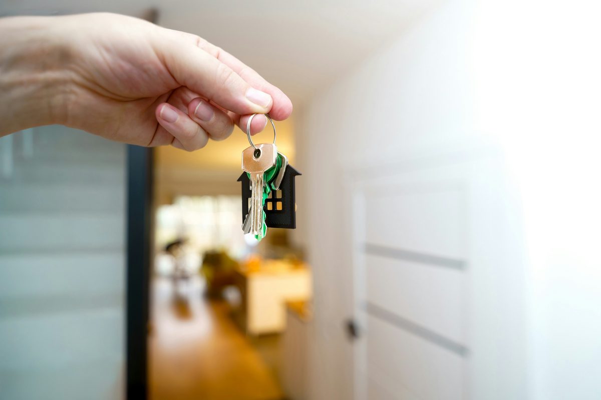 Mano entregando las llaves de una vivienda delante de la puerta