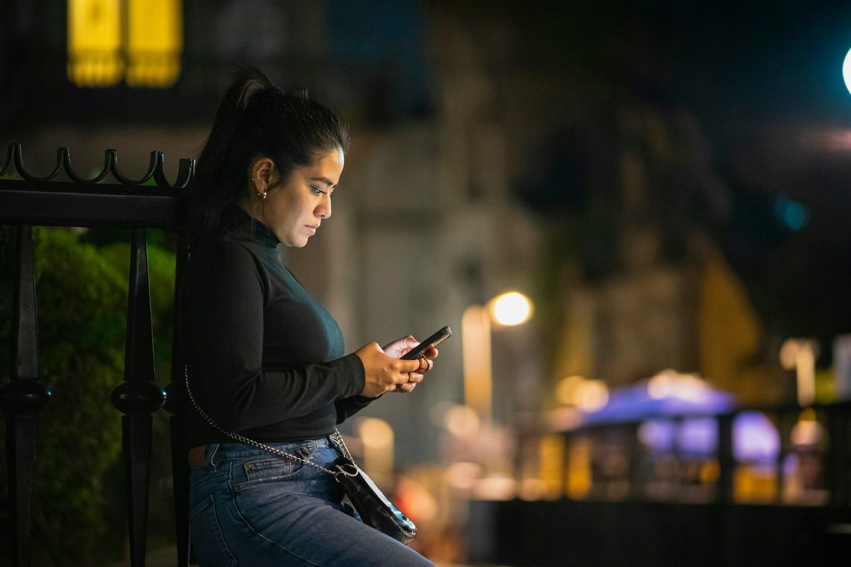 Mujer mirando el móvil en la calle, de noche