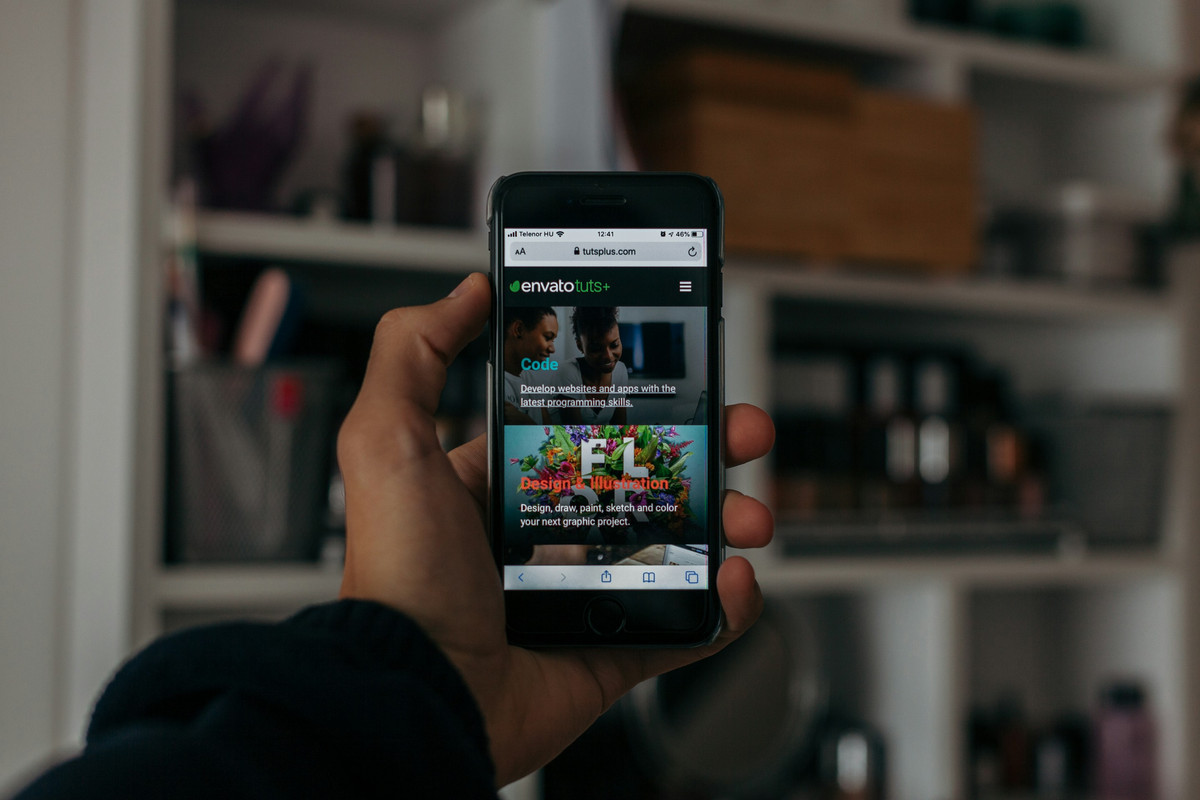 Mano con un móvil que enseña una página web, delante de unas estanterías