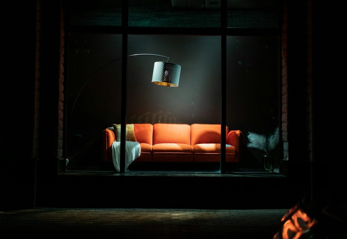 Escaparate iluminado de noche con un sofá naranja