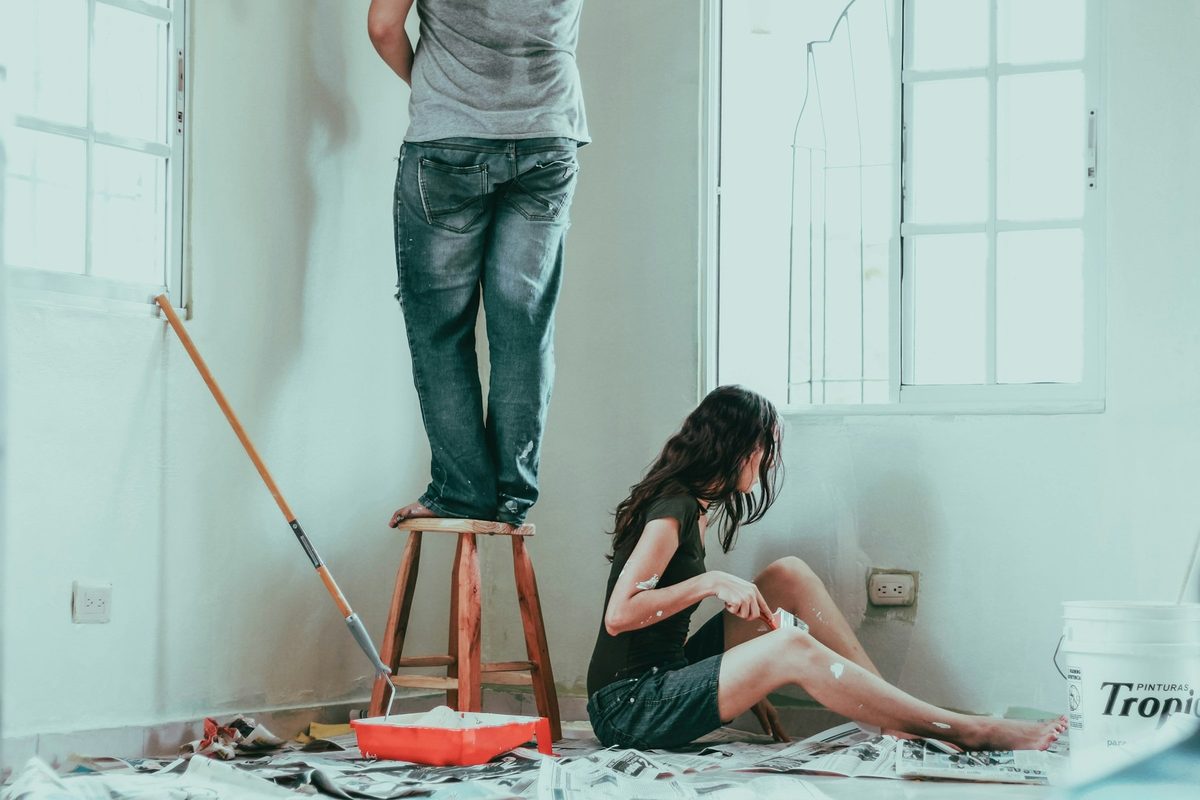 Pintor trabajando subido a un taburete mientras una mujer espera sentada en el suelo