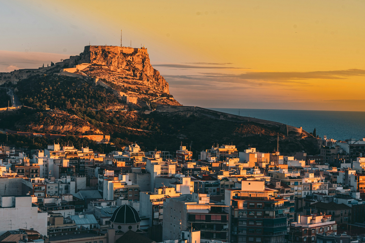 El castillo de Santa Bárbara sobre el monte Benacantil al atardecer, con los edificios de Alicante debajo y el mar al fondo