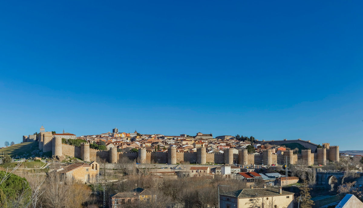 Vista panorámica de Ávila con la muralla medieval entera rodeando el casco antiguo, bajo un cielo azul