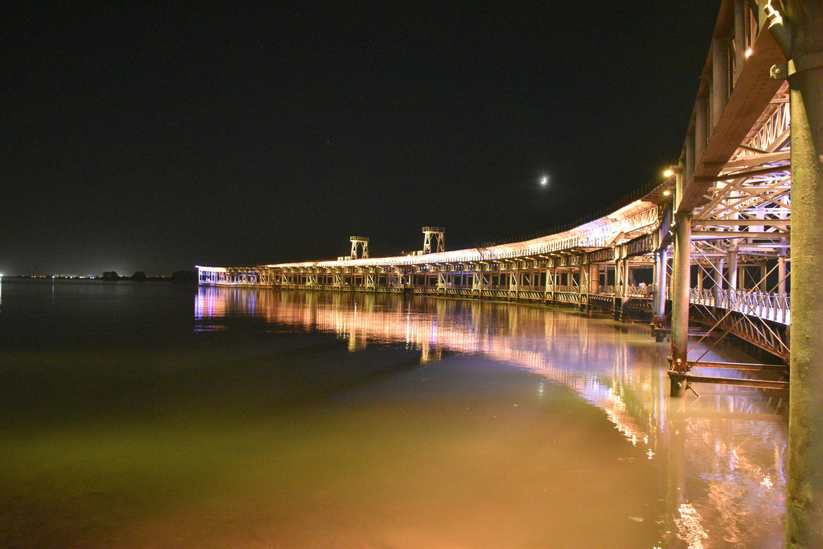El muelle del Tinto de Huelva iluminado de noche y reflejado en la ría